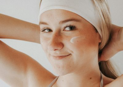 Mujer joven con vincha blanca sonriendo en tratamiento facial.